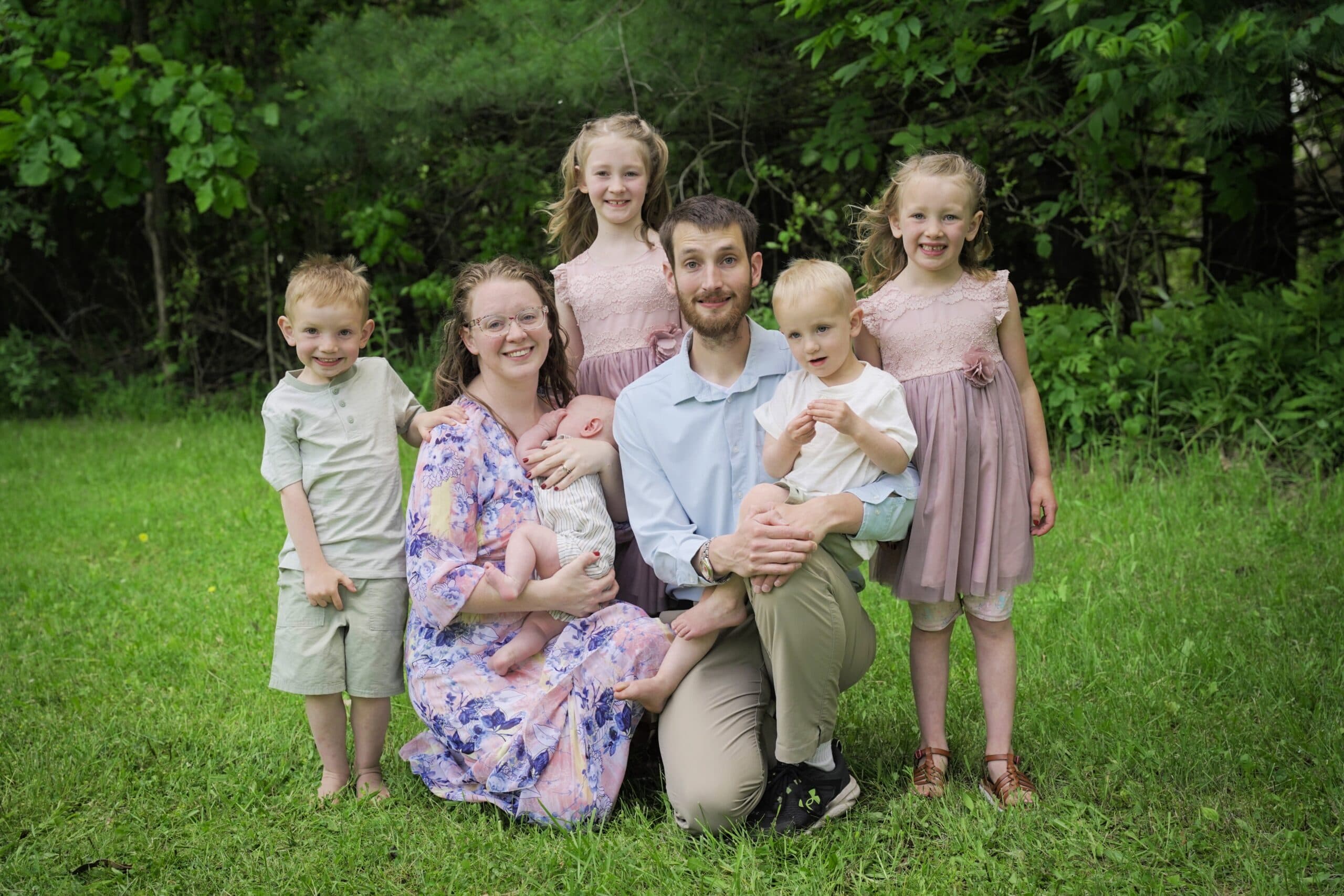 Pastor Virgil Ruchti and his wife Cynthia on the grass with their six children, the youngest still an infant, trees behind them